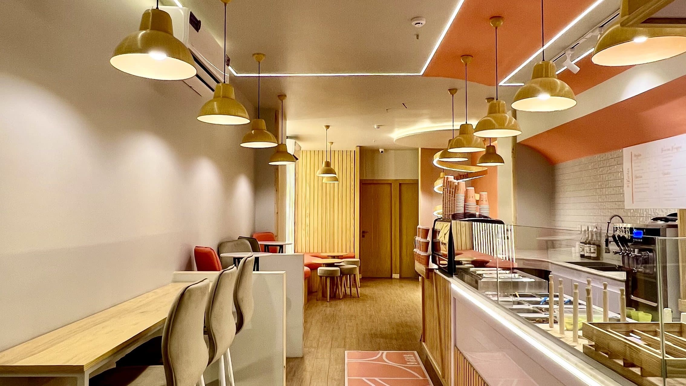 Completed Kurtos cafe interior in Islamabad showing the service counter, pendant lighting, timber finishes, linear ceiling lights and spiral brand feature.