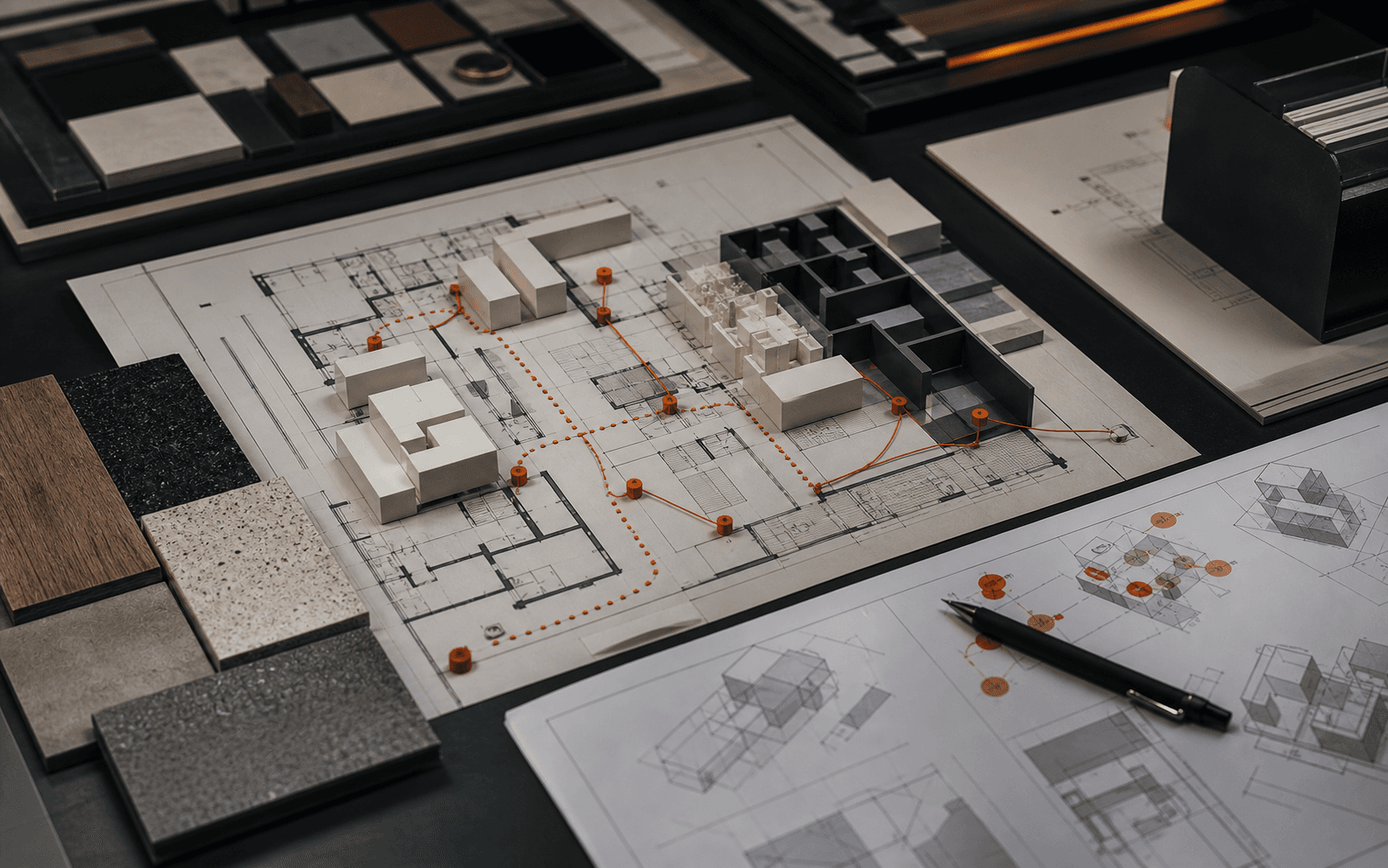 Close editorial view of architectural plans, massing blocks, material samples, and orange pins mapping public and service routes.