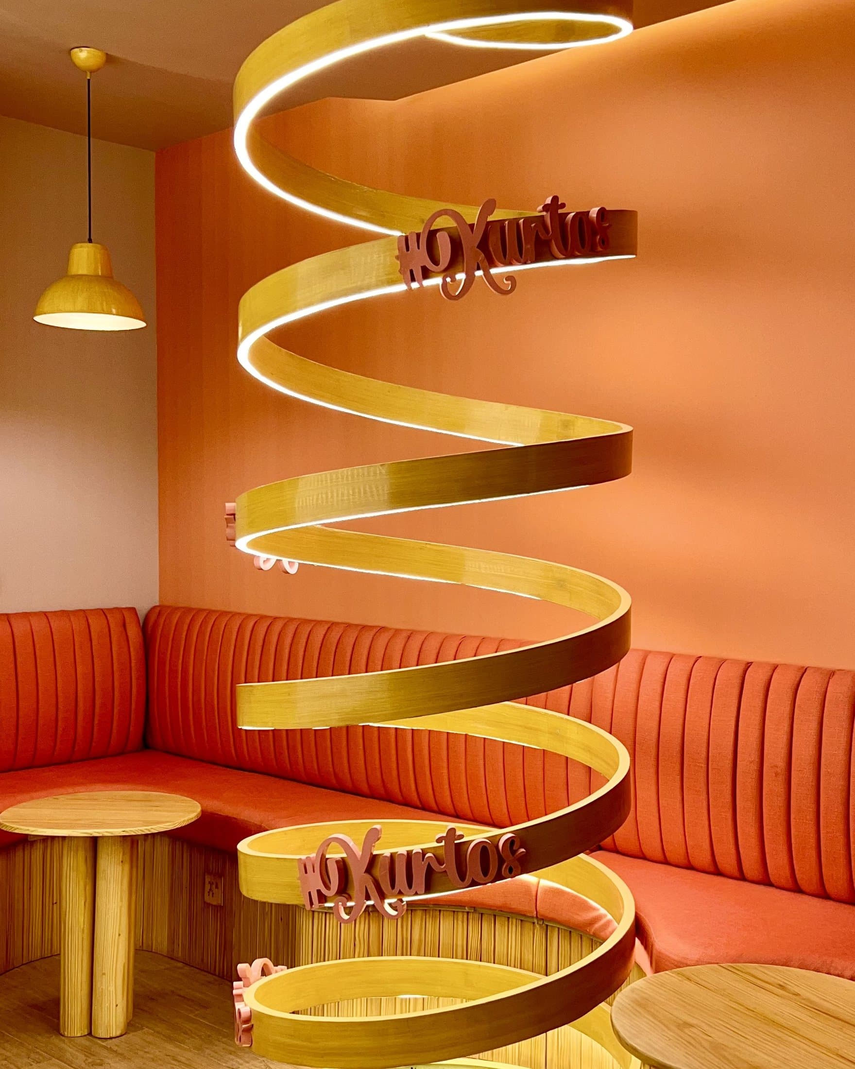 Completed Kurtos spiral brand feature with illuminated timber bands, orange upholstery and pink Kurtos lettering.