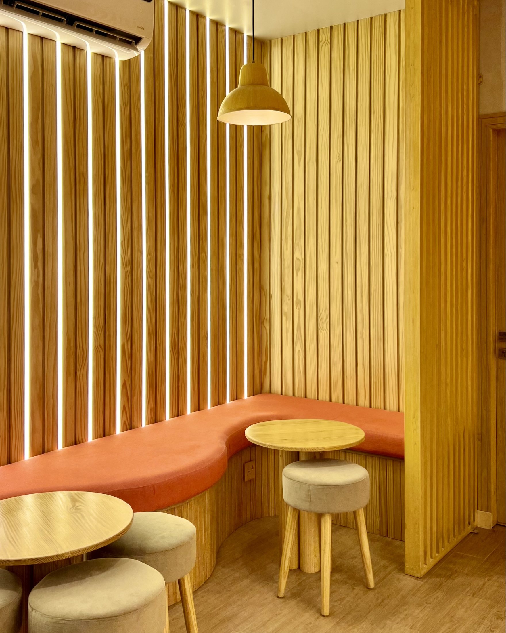 Completed Kurtos corner banquette with timber slats, vertical linear lighting, orange upholstery and round timber tables.