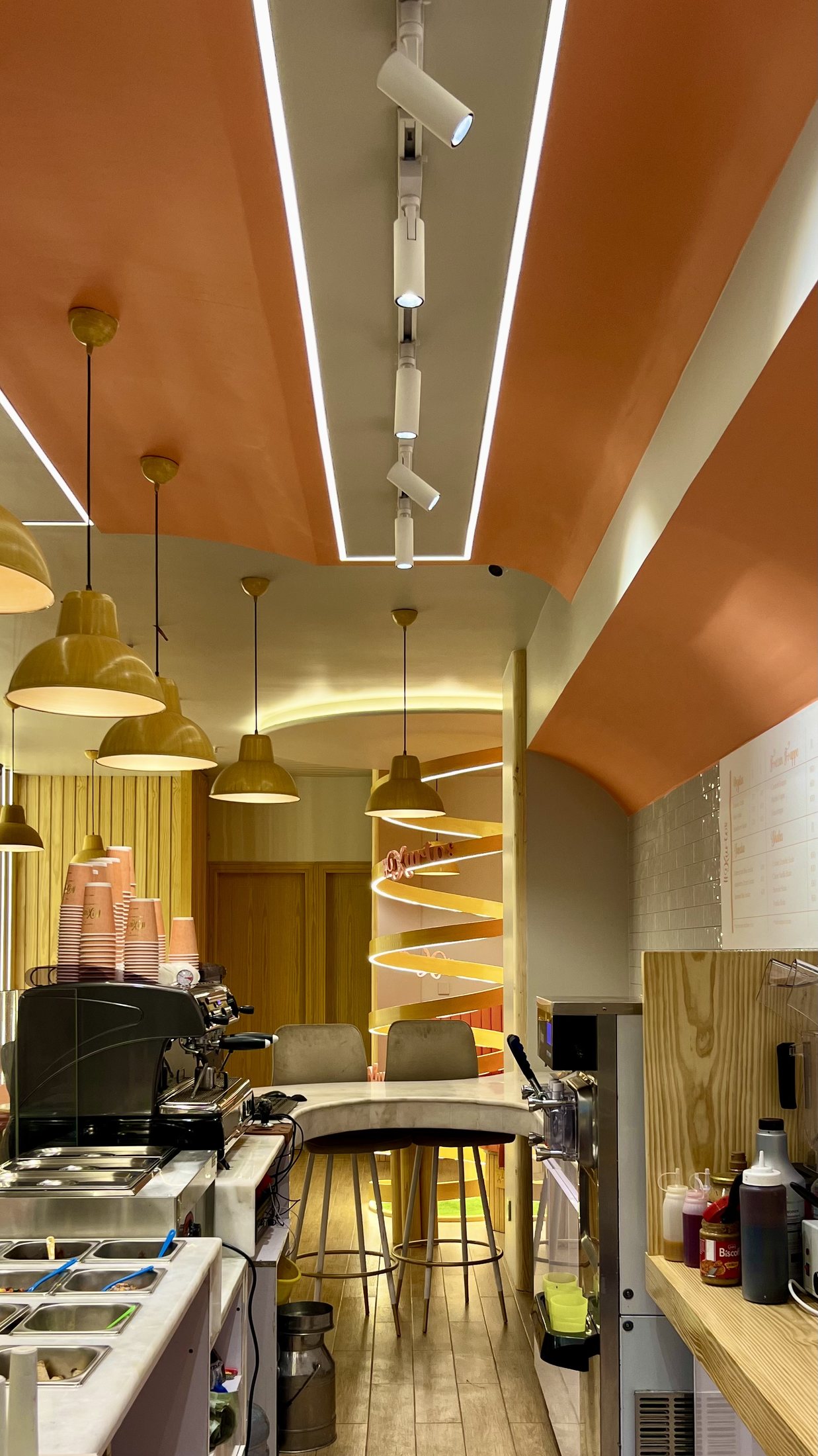Completed Kurtos service lane looking upward to orange ceiling bands, linear lights, track lights and pendant fixtures.