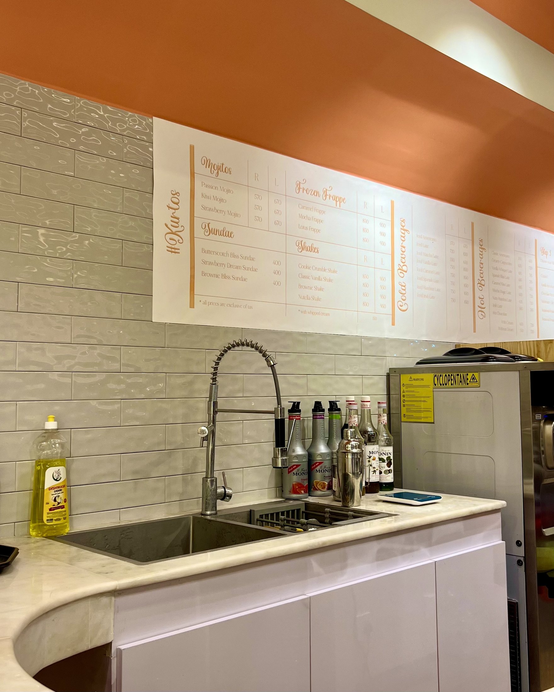 Completed Kurtos menu and service counter wall with pale tile, marble counter and orange overhead band.