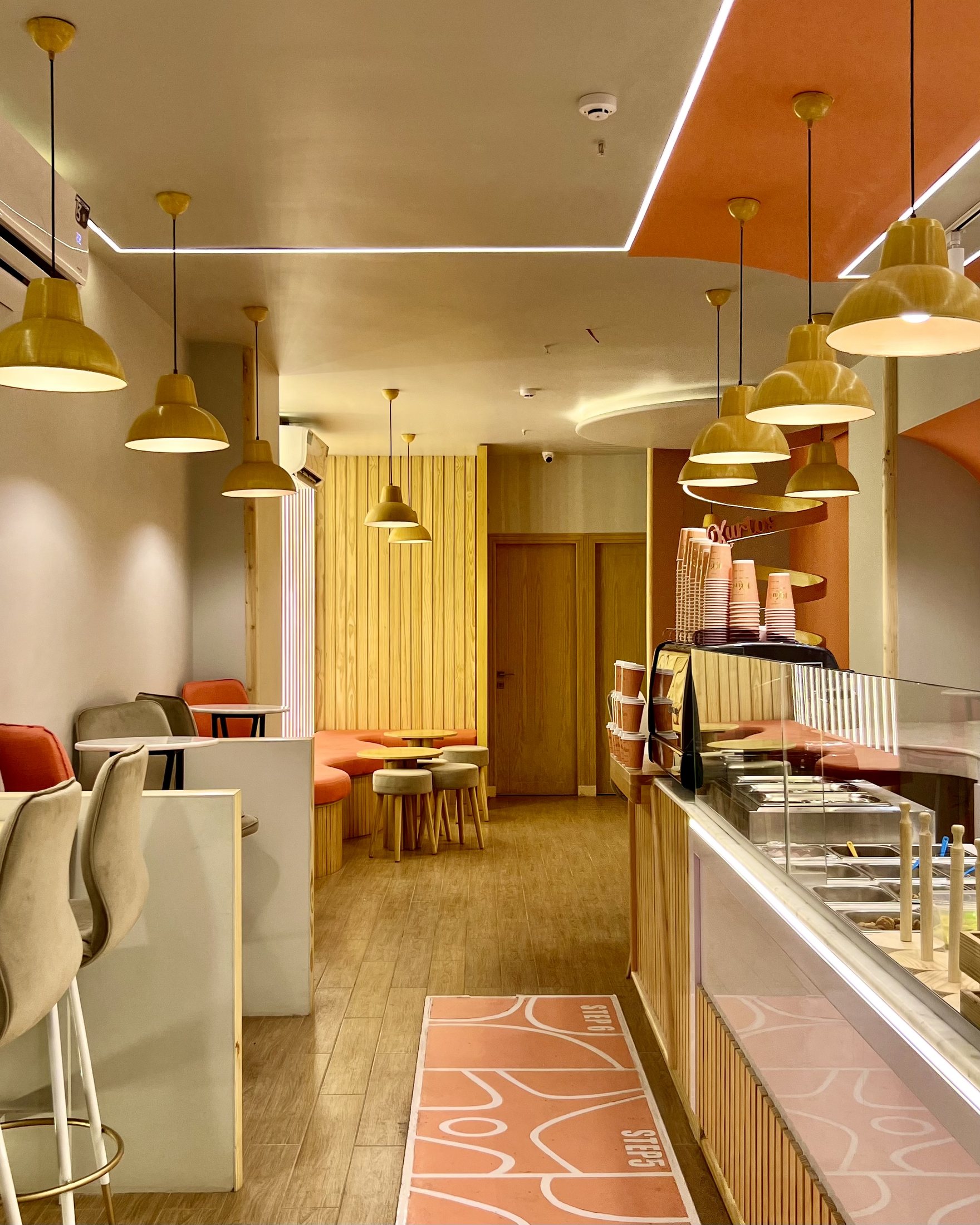Completed Kurtos interior showing the service counter, seating lane, pendant lights, timber wall panels and illuminated ceiling lines.