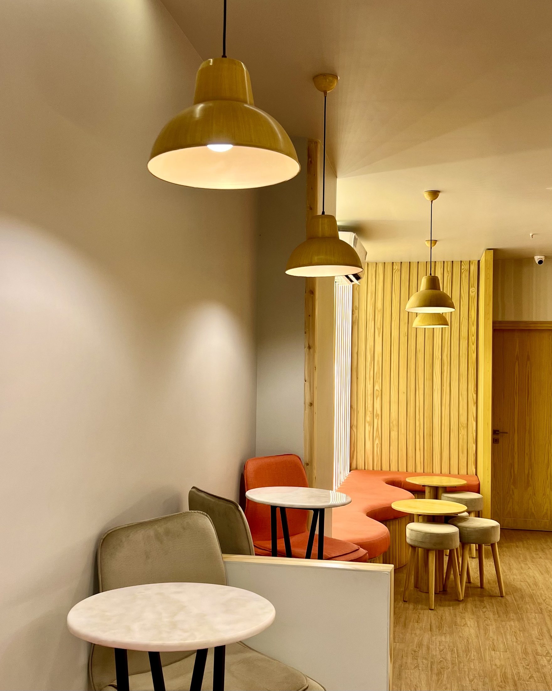 Completed Kurtos seating zone with orange banquette, timber wall panels, pendant lighting and compact tables.