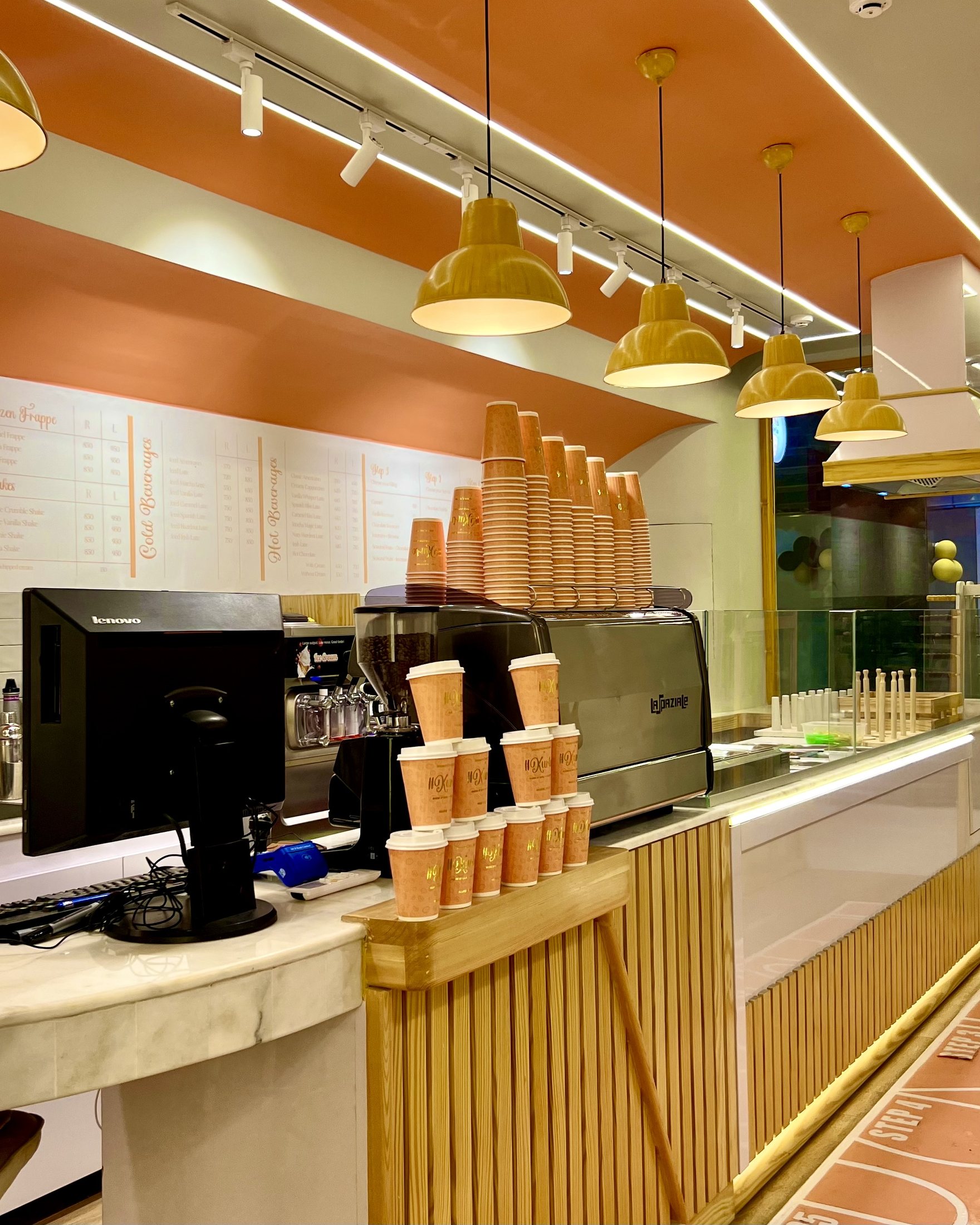 Completed Kurtos service counter with coffee equipment, cup display, timber cladding, marble counter and pendant lighting.