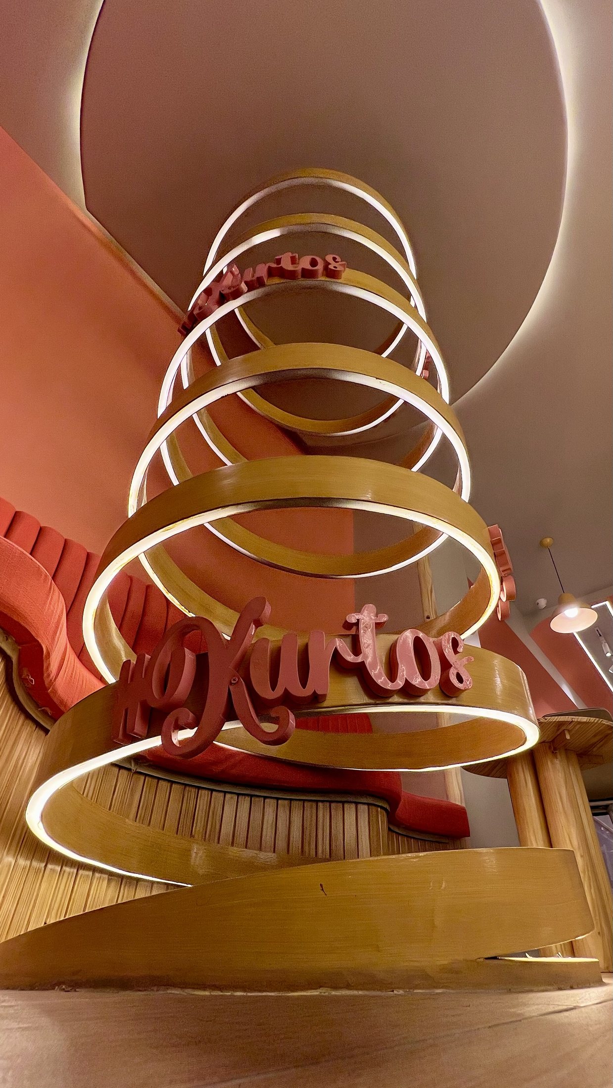 Completed Kurtos spiral detail looking upward through illuminated timber bands and brand lettering.