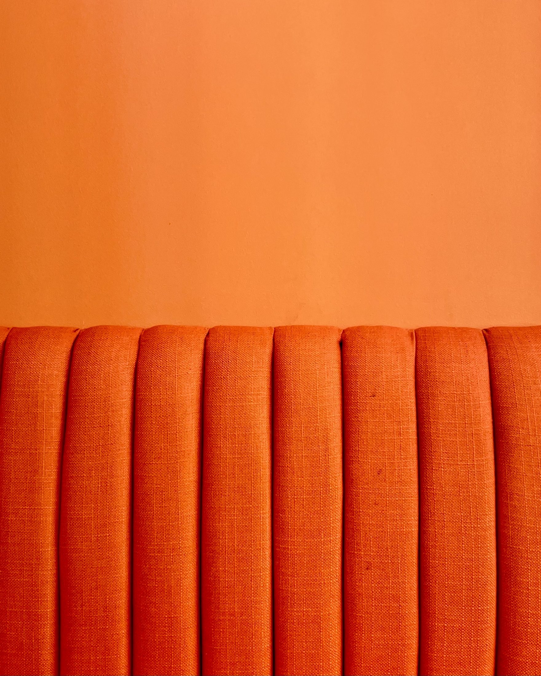 Completed Kurtos orange upholstered backrest detail against a matching painted wall.